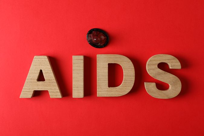 Word AIDS and condom on red background, space for text