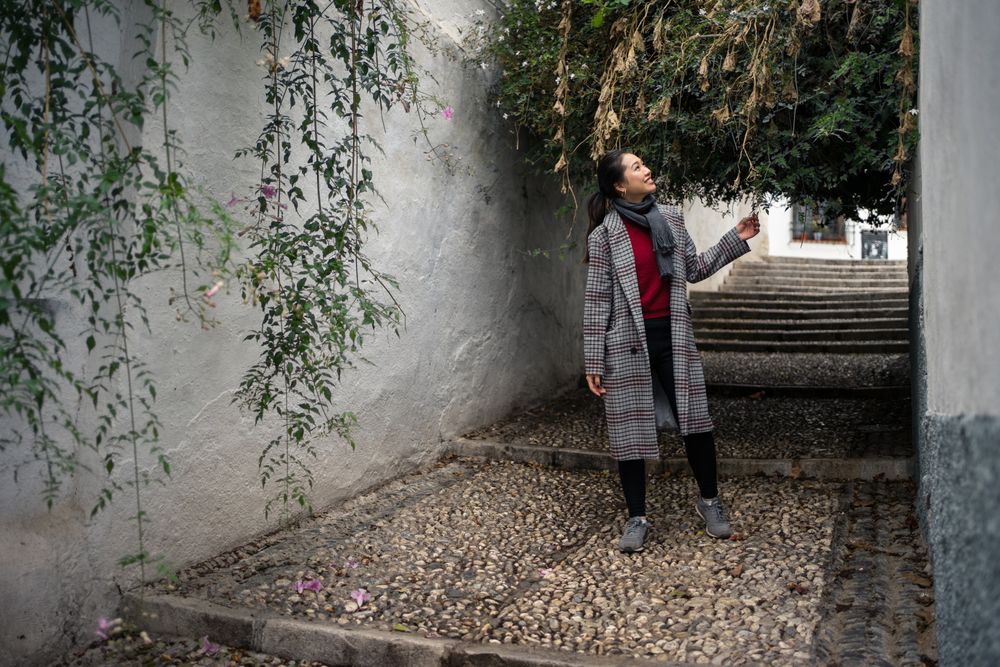 Young female in casual clothing touching green plants and smiling at rocked lane