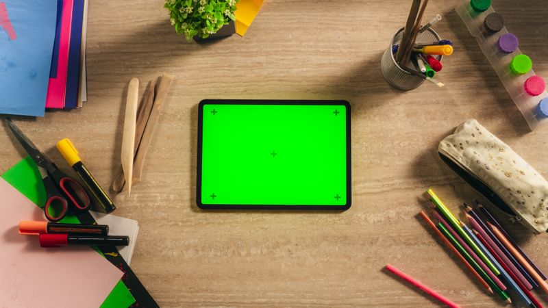 Top Down View of a Tablet Computer with Mock Up Green Screen Display. Device Lying Horizontally on a Table in a Creative Kids Room. Template for Online Digital Marketing, Social Media Promotion