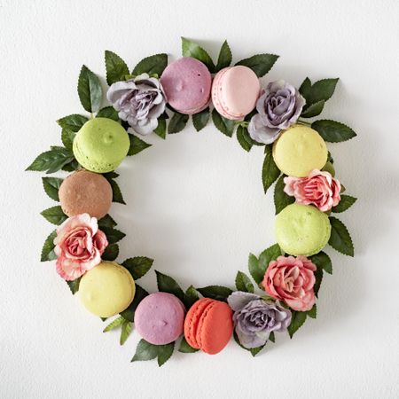 Pink and purple flowers and leaves with macarons in wreath on light  background