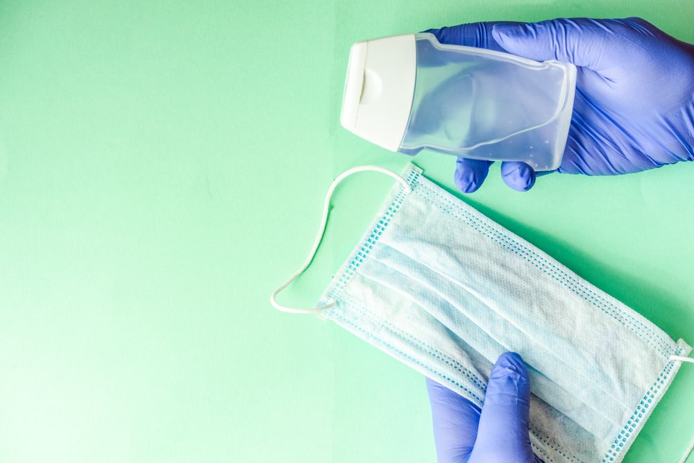 Covid-19 virus concept of hands in latex gloves holding facemask and bottle of anti bacterial wash