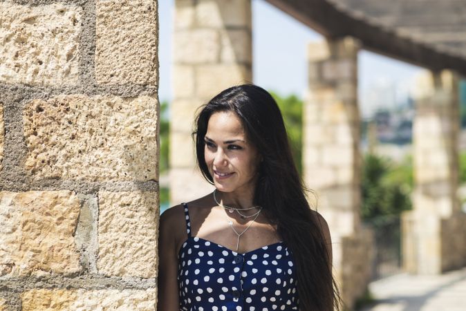 Calm woman in blue dress leaning on wall while wistfully looking away