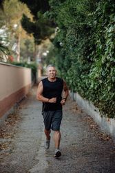 Older man in good shape running on road along plant fence
