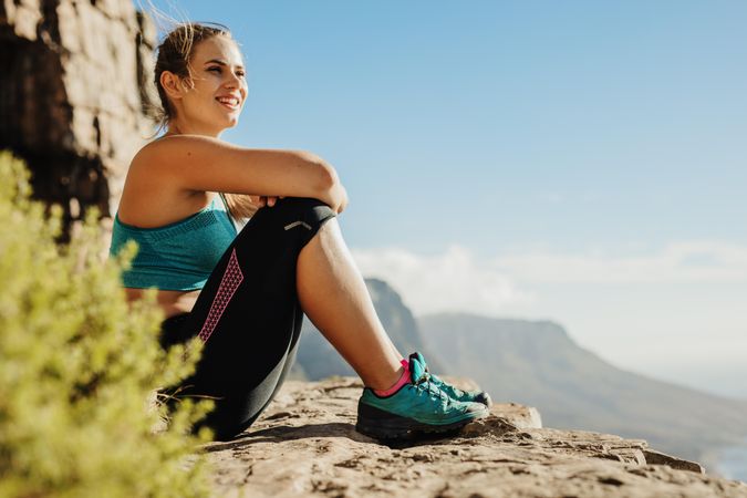 Fitness woman sitting on a cliff looking at the view and smiling