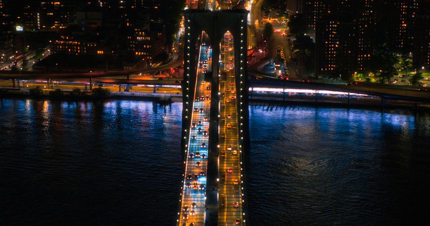 New York City Skyline Aerial Image from a Helicopter at Night. Famous Skyscraper Buildings and Brooklyn Bridge with Illuminated American Flags. Busy Diverse Megapolis with Cars, Traffic, Nightlife