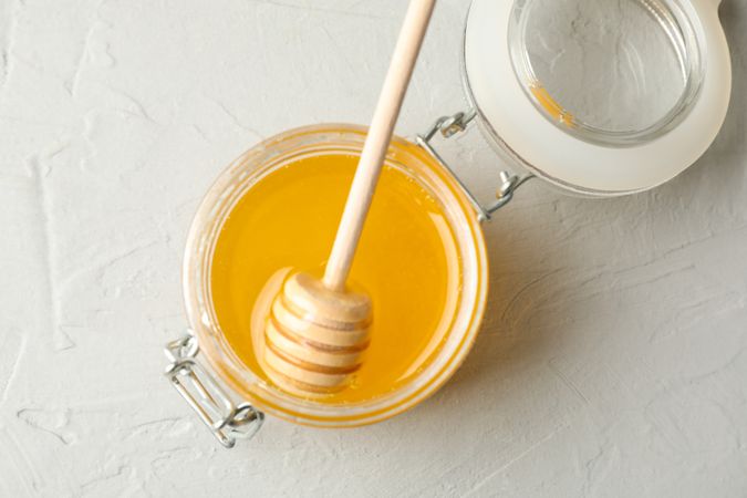 Glass jar with honey and dipper on neutral background, top view