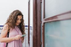 Woman with smartphone and headset beside entrance