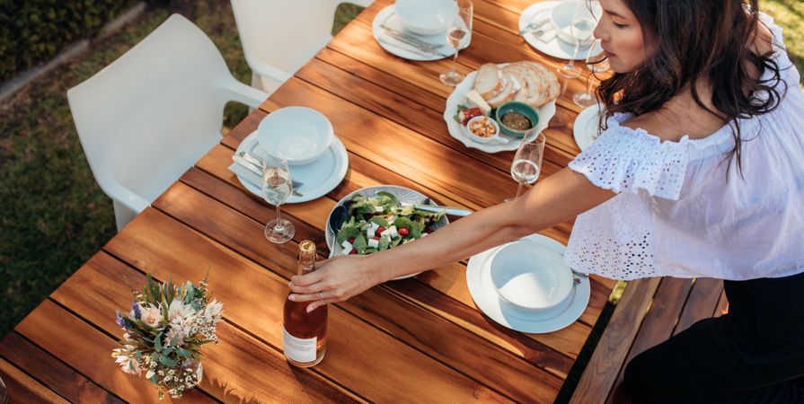 Female setting a dining table outdoors with food and drink