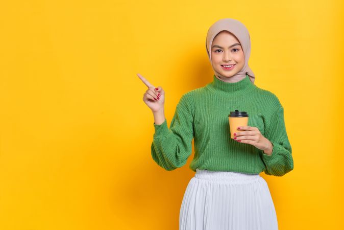 Woman in headscarf holding to go coffee cup and pointing upwards