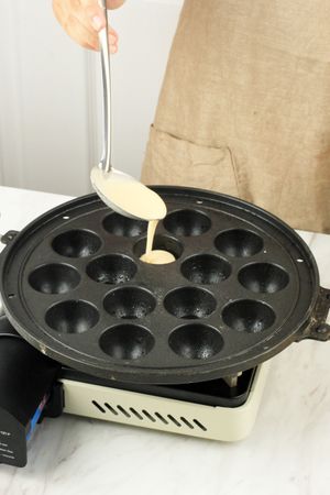 Person spooning batter into bubble waffle maker for Japanese dish