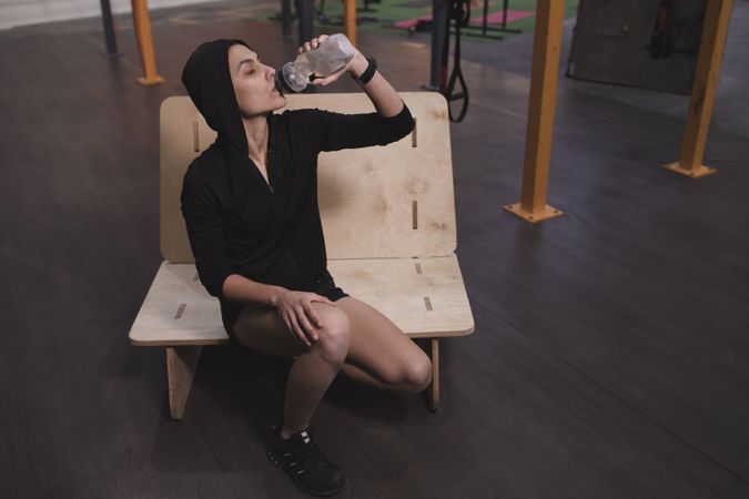 Smiling woman drinking with bottle of water in gym