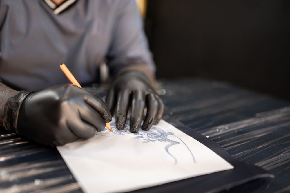 A tattoo artist is drawing a design stencil on his work stretcher before tattooing
