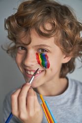 Smiling boy painting rainbow on face