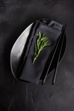 Minimalistic table setting in dark color with rosemary sprig