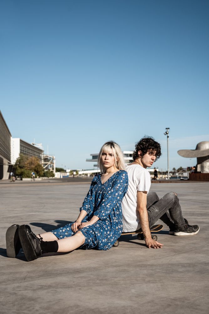 Trendy couple sitting together on skateboard on street