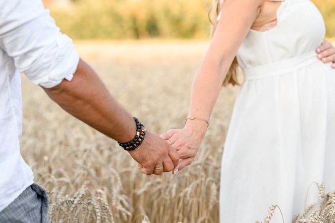 Anonymous couple holding hands and standing in wheat field