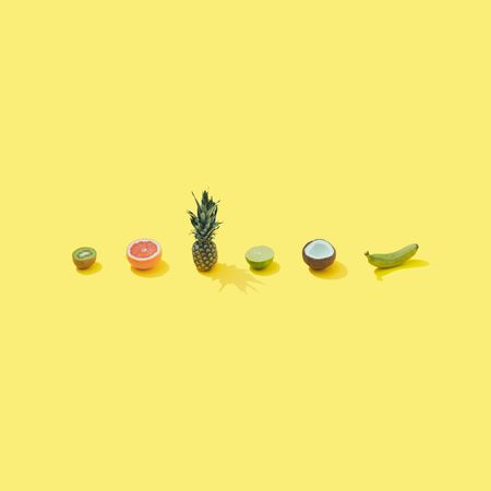 Row of tropical fruit on pastel yellow background