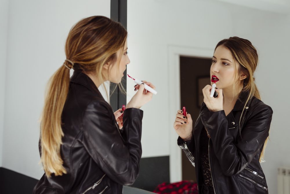 woman applying lipstick near mirror at home