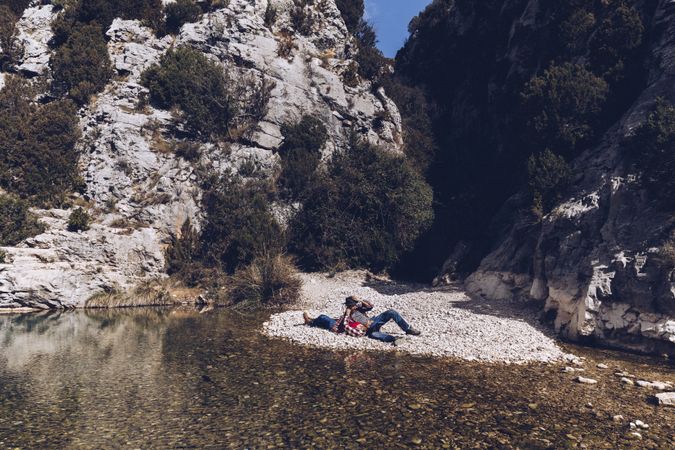 Positive woman and man resting on stone shore near river