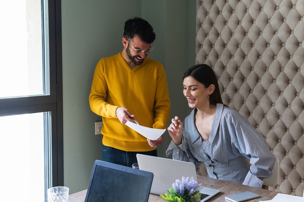 Cheerful colleagues discussing data on paper sheet in office