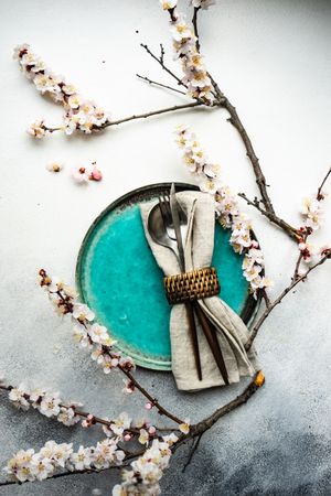 Table setting with delicate apricot blossom around elegant teal tableware on grey counter