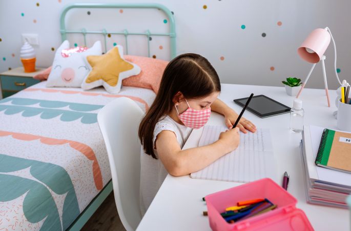 Girl with mask doing homework in her bedroom