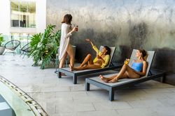 Two women friends laugh while resting on a lounge seat when they unexpectedly run into an acquaintance