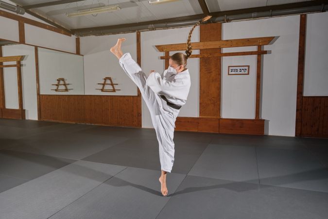 Woman wearing a mask with a white kimono kicking in the air