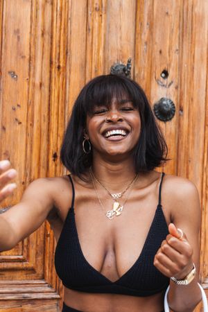 Cheerful Black woman in black outfit against wooden wall