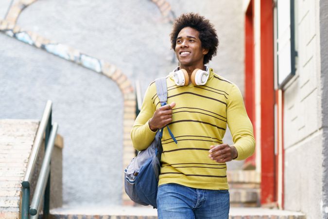 Relaxed man in yellow shirt and headphones walking down stairs outside