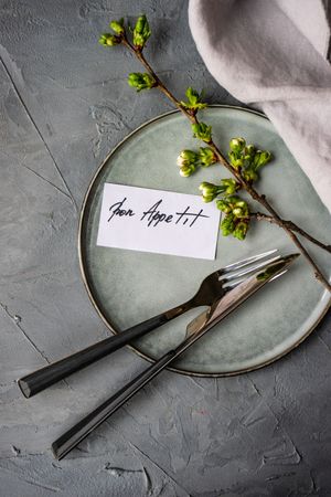 Bon appetit note on plate with cherry blossom, knife and fork, vertical composition