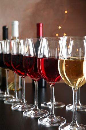 Bottles and glasses with wine on dark table, blurred lights, closeup