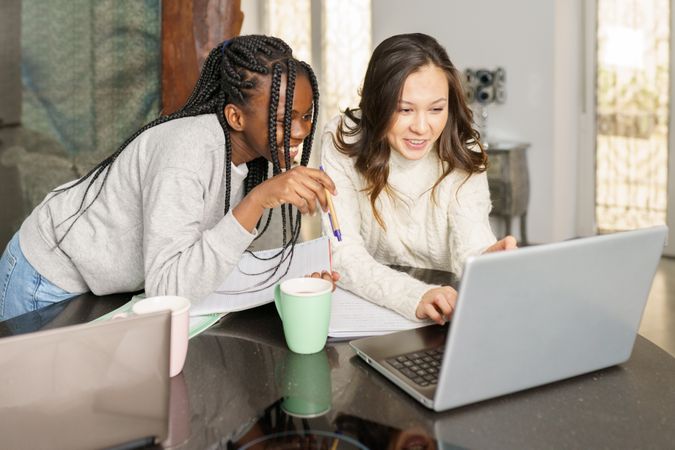 Two women sitting at kitchen table smiling at something on a pc