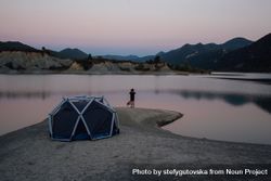 Man and dog looking over lake with tent at sunset beOwl5