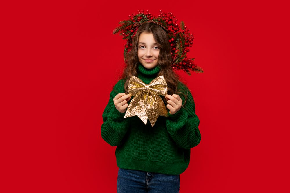Young girl in green sweater holding large golden glittery bow