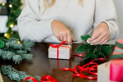 An unrecognizable woman is wrapping a Christmas gift in craft paper and a fir branch