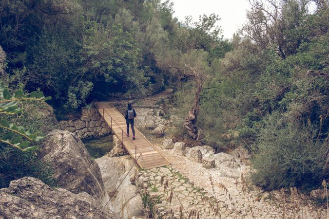 Unrecognizable female backpacker walking on wooden footbridge in