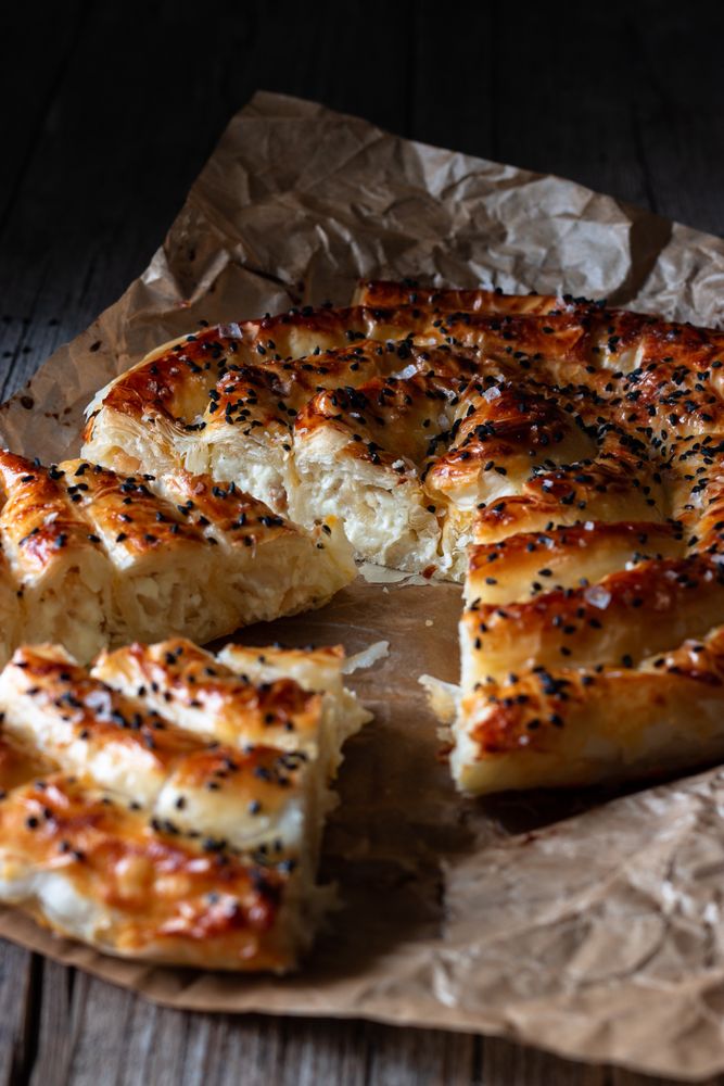 From above crop cook holding hot baking dish with fresh puff pastry and serving piece of borek on plateFrom above crop cook holding hot baking dish with fresh puff pastry and serving piece of borek on plate
