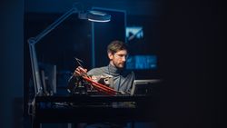Professional Automotive Engineer in Glasses and Inspection Tools is Testing an Used Electric Engine in a High Tech Laboratory at Night.