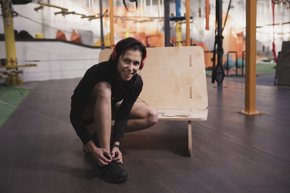 Smiling woman with headphones lacing shoe in gym