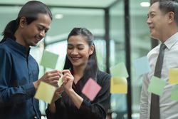 Male and female brainstorming with sticky notes in office with manager looking on