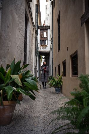 Female traveler in casual clothing at alley with quick pot of flowers
