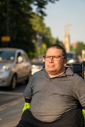 Man sitting in wheelchair on sidewalk in busy city, vertical