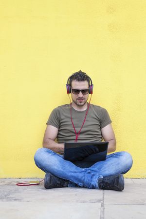 Man with red headphones sitting outside looking at laptop