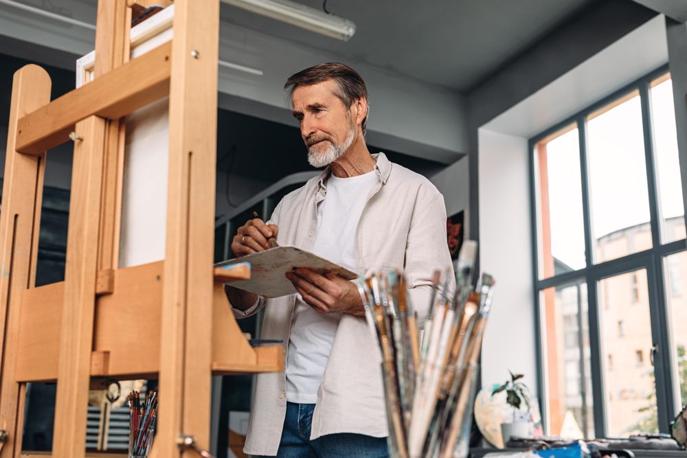 Man in grey beard with paint brushes in his studio