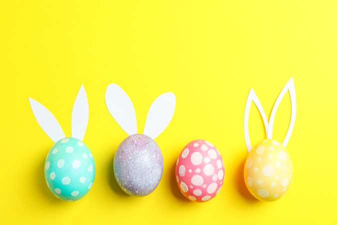 Decorated Easter eggs with cute bunnies ears on yellow background. Space for text