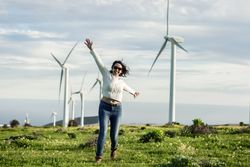 Happy woman in light sweater and denim pants standing beside wind turbines