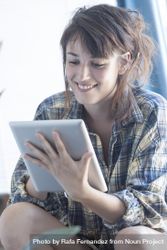 Smiling female in flannel shirt lounging in bright room with digital tablet bGaWl5