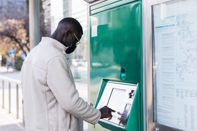 Black businessman touching screen of ATM in town