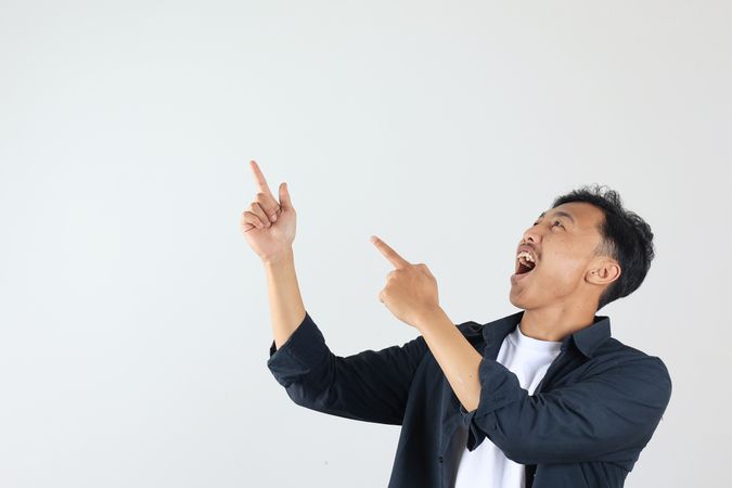 Excited Asian Indonesian man with Blue Shirt Pointing on Empty Space on Left Above